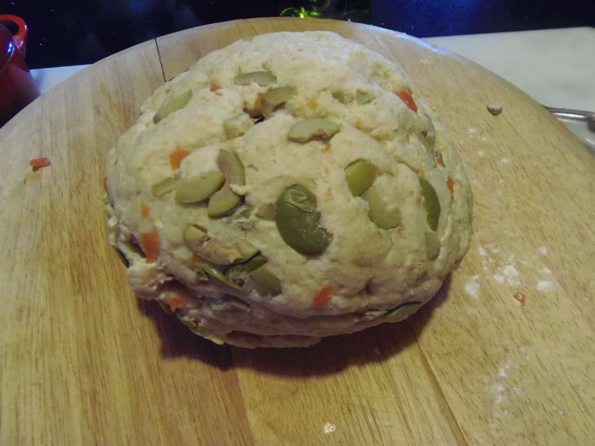 Chopped pimento olives in a ball of dough on a wooden board.