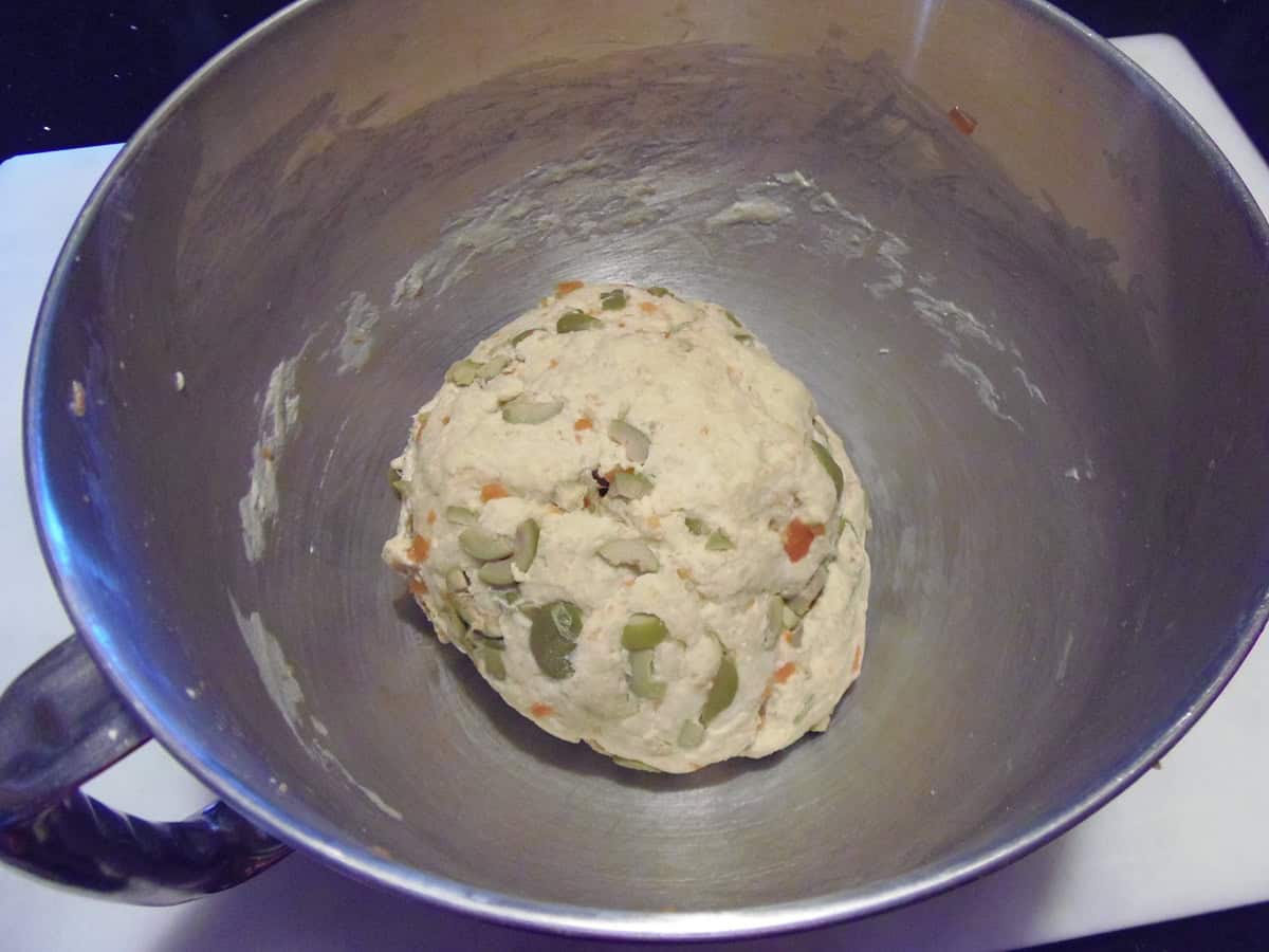 An unproved ball of olive bread dough in the bowl of a stand mixer.