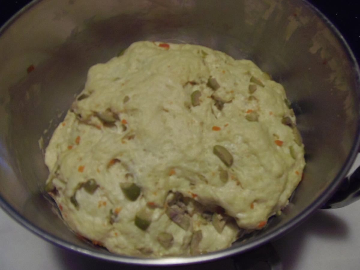 A proved ball of olive bread dough in a stand mixer bowl.