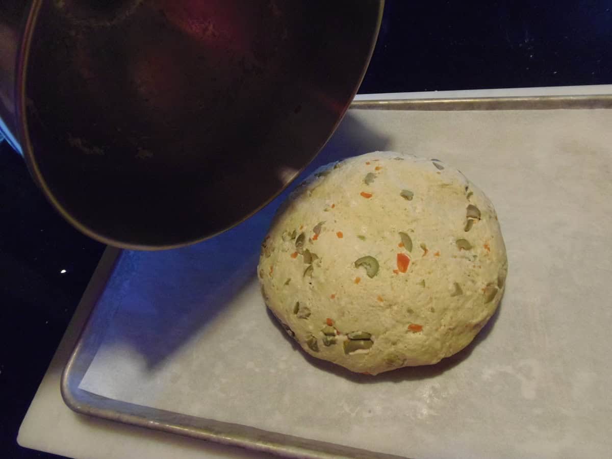 A dough ball of rustic olive bread being turned out onto a parchment lined baking sheet.