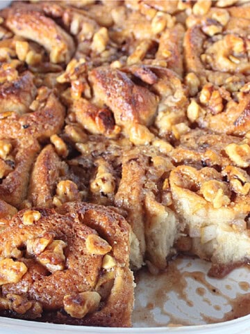 A bunch of rolled yeast buns with pears and chopped walnuts in a baking pan.