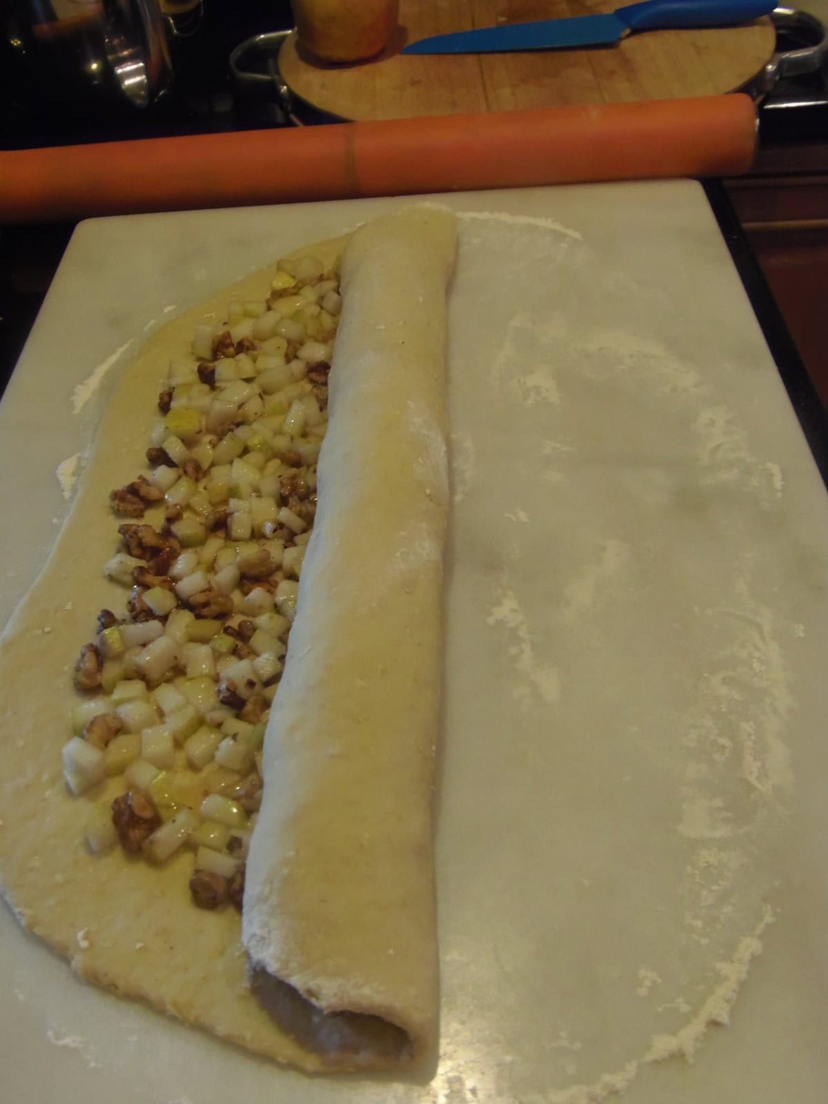 A flattened roll of dough being rolled with filling.
