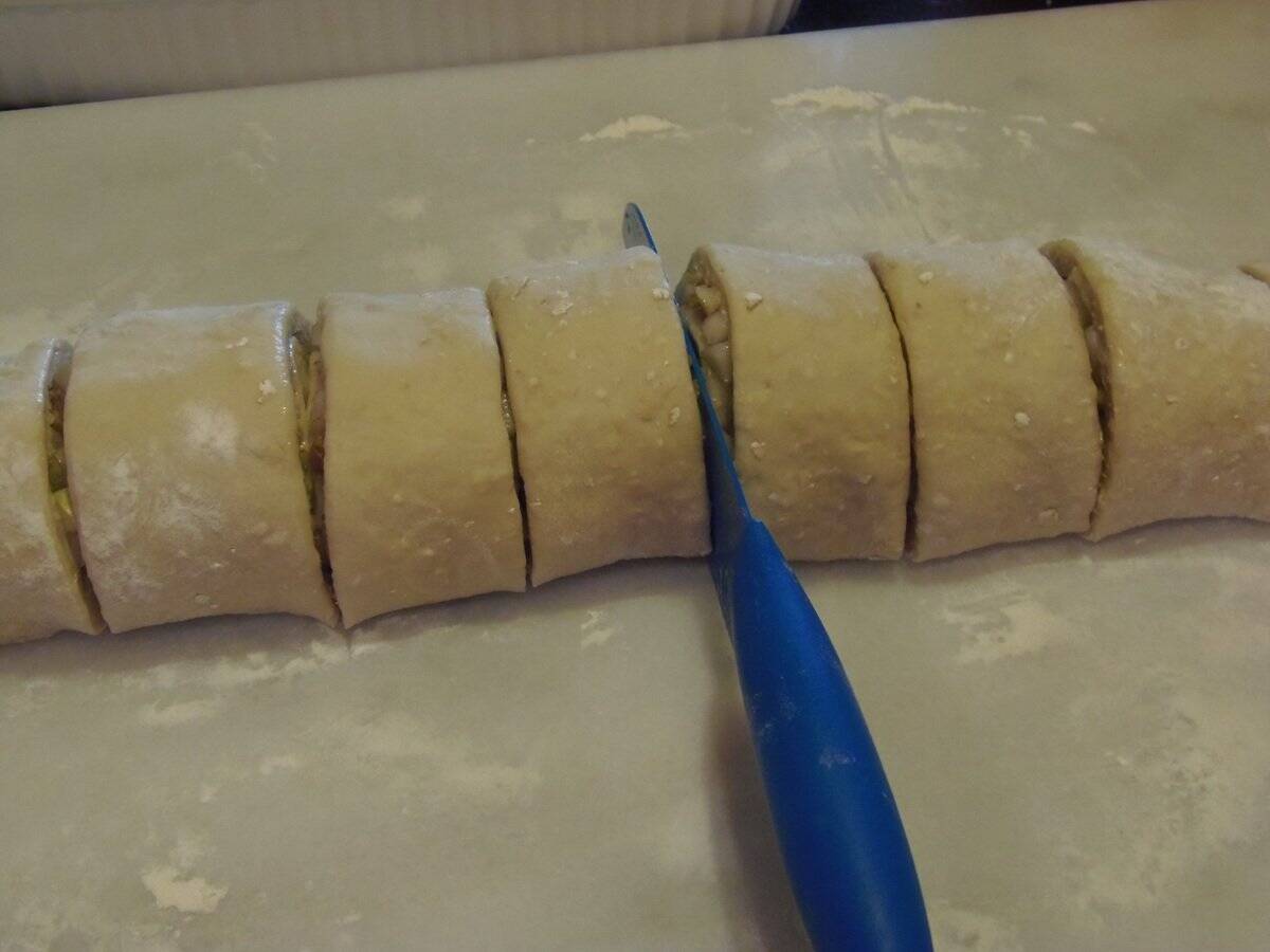 A sliced roll of unbaked pear and walnut sticky buns before being added to a baking dish.