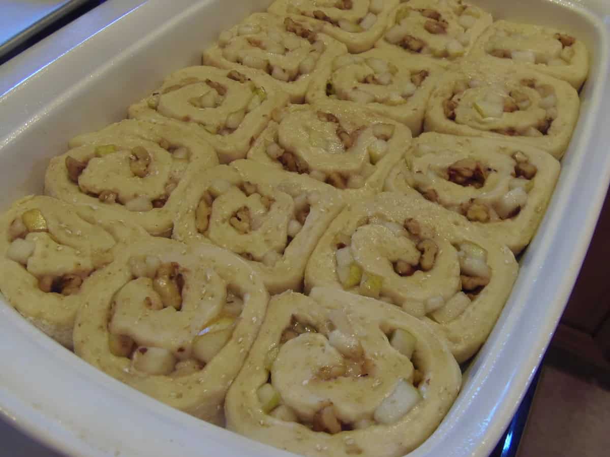 Swirled and unbaked sticky buns in a white baking dish.
