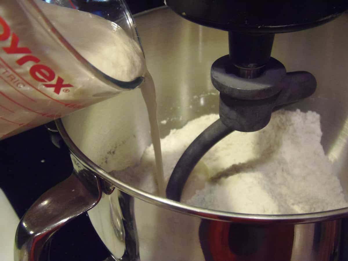 Foamy yeast mixture being added to a stand mixer bowl.
