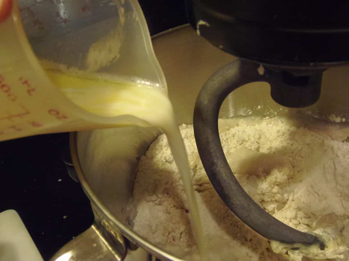 Melted butter being poured into a stand mixer bowl for making dough.