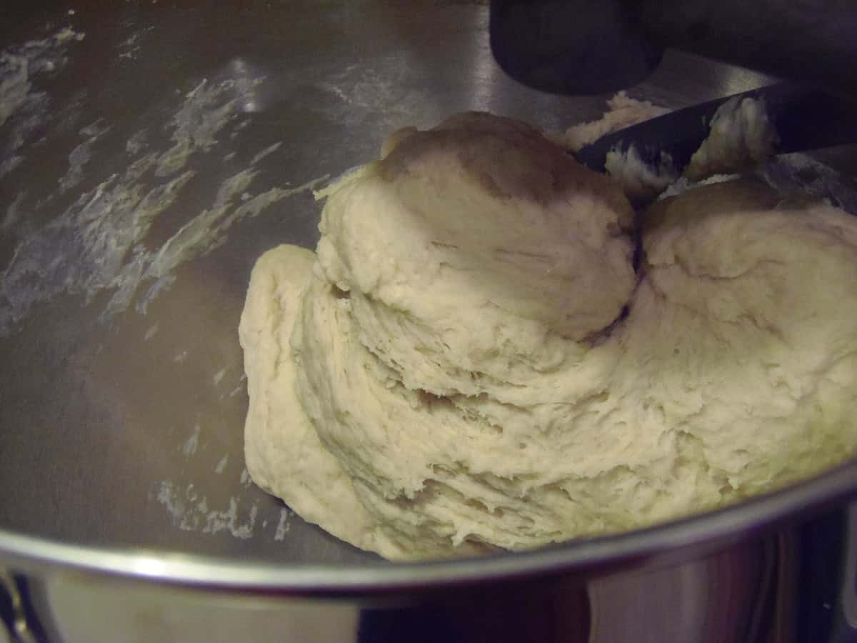 A soft dough being kneaded with a dough hook in a stand mixer bowl.
