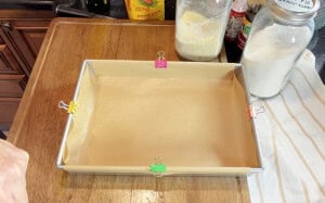 A 9 x 13 baking dish lined with parchment paper sheets and held in place with metal clips.