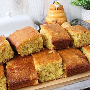 A pile of golden brown squares of cornbread with a butter dish and honey jar in the background.
