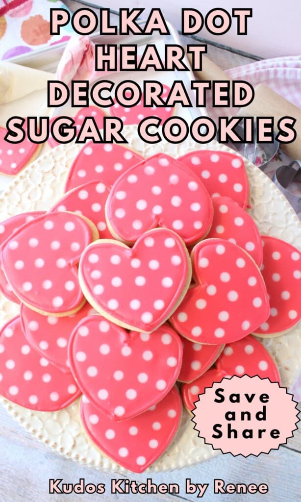 A stack of pink and white Polka Dot Heart Decorated Sugar Cookies on a pretty white cake stand.