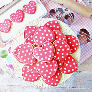 A pretty stack of pink polka dot heart decorated sugar cookies on a white cake stand.