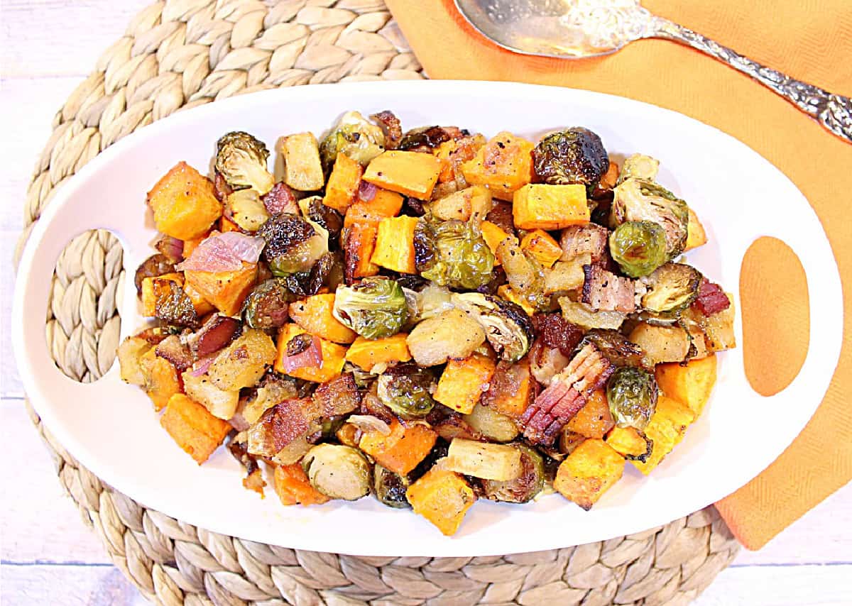 Sweet and Savory Roasted Sweet Potatoes, Brussels Sprouts and Apples - Kudos Kitchen by Renee A silver spoon and napkin on the side of a bowl filled with roasted seasonal vegetables.