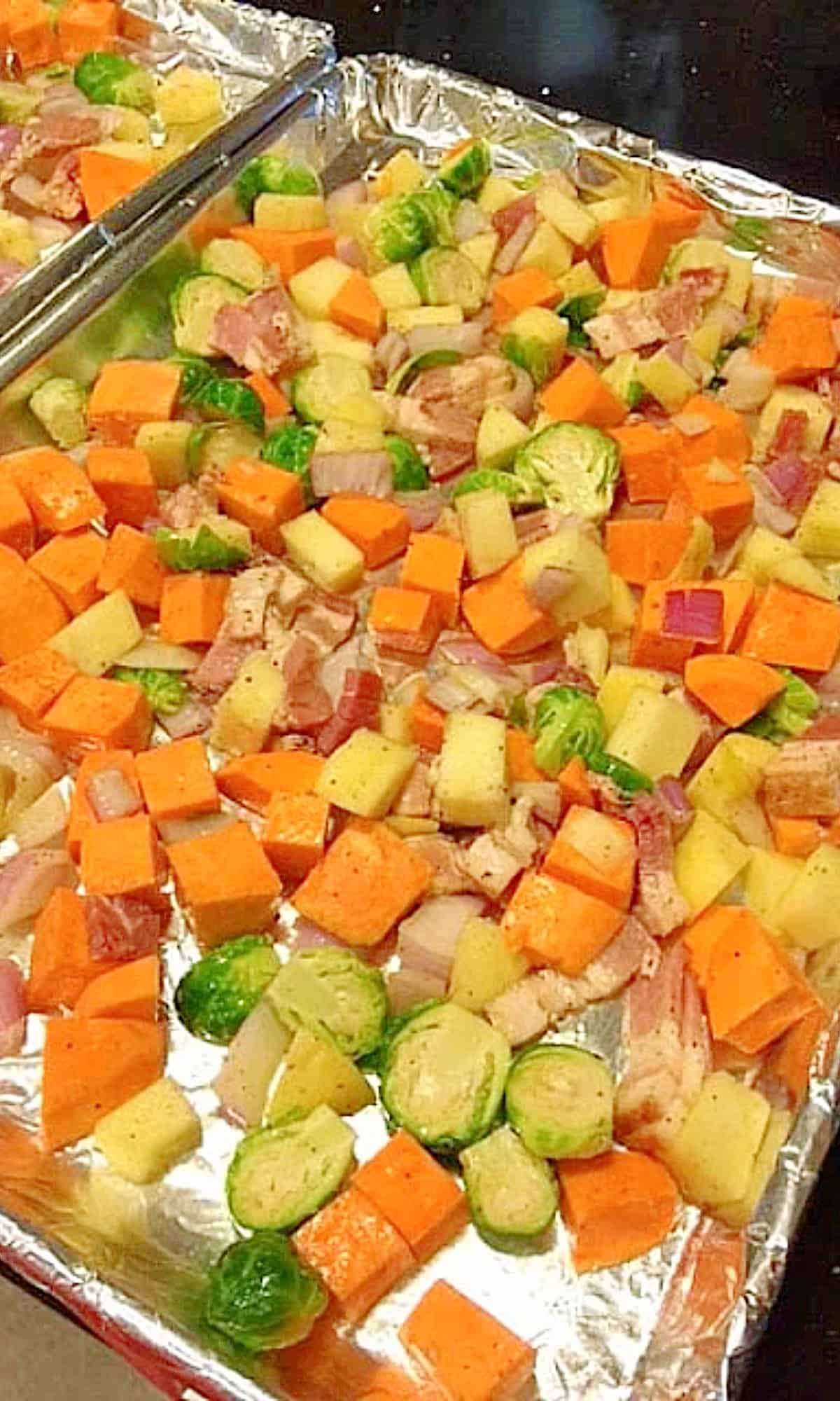 Fall's bounty of flavors and colors shine brightly in this dish of Sweet Savory Roasted Sweet Potatoes Brussels Sprouts with Apples. - Kudos Kitchen by Renee - kudoskitchenbyrenee.com Chopped sweet potatoes and Brussels sprouts along with apples on a foil lined baking sheet ready to go into the oven.