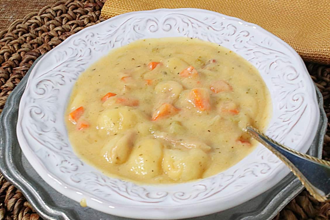 A pretty white bowl filled with golden creamy gnocchi soup with cheddar and bacon along with a spoon.