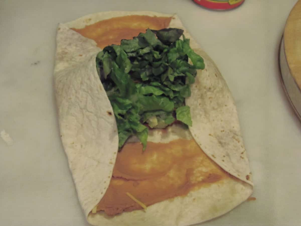 Two ends of a flour tortilla being folded over the filling to make a wrap.