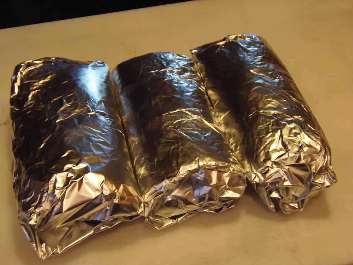 Three chicken and avocado wraps wrapped in foil.