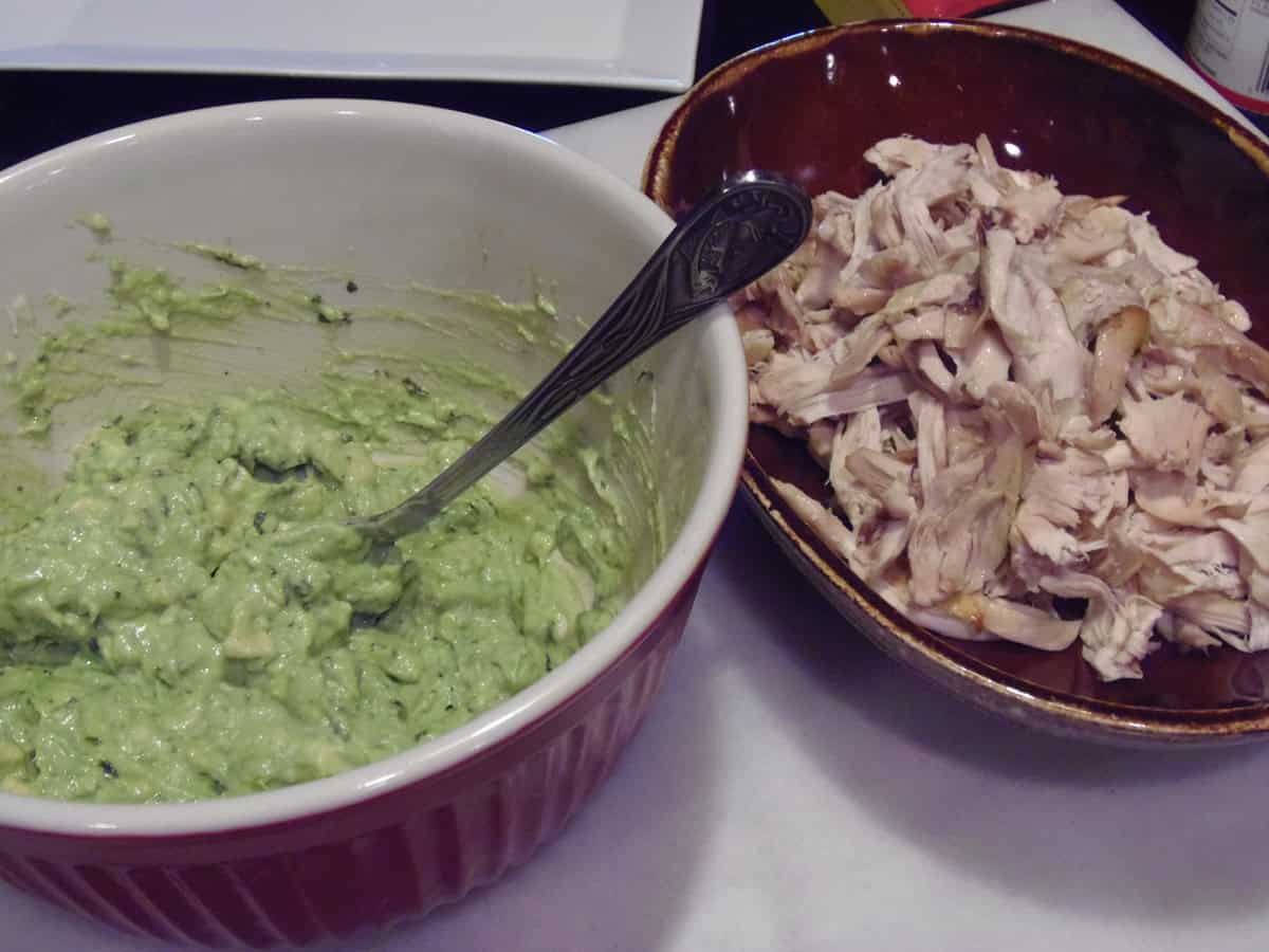 A bowl of mashed avocado next to a brown bowl filled with shredded rotisserie chicken.