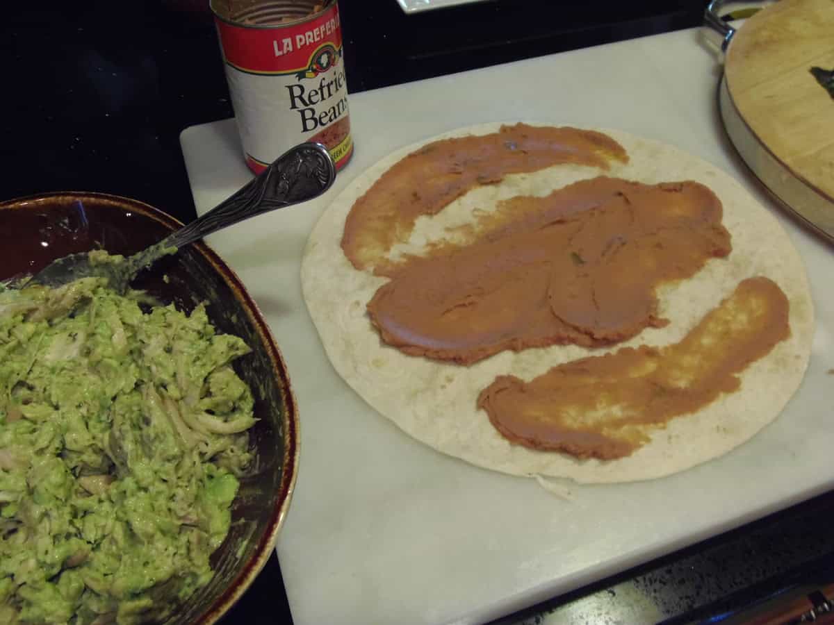 Swipes of refried beans spread across a flour tortilla to make a wrap.