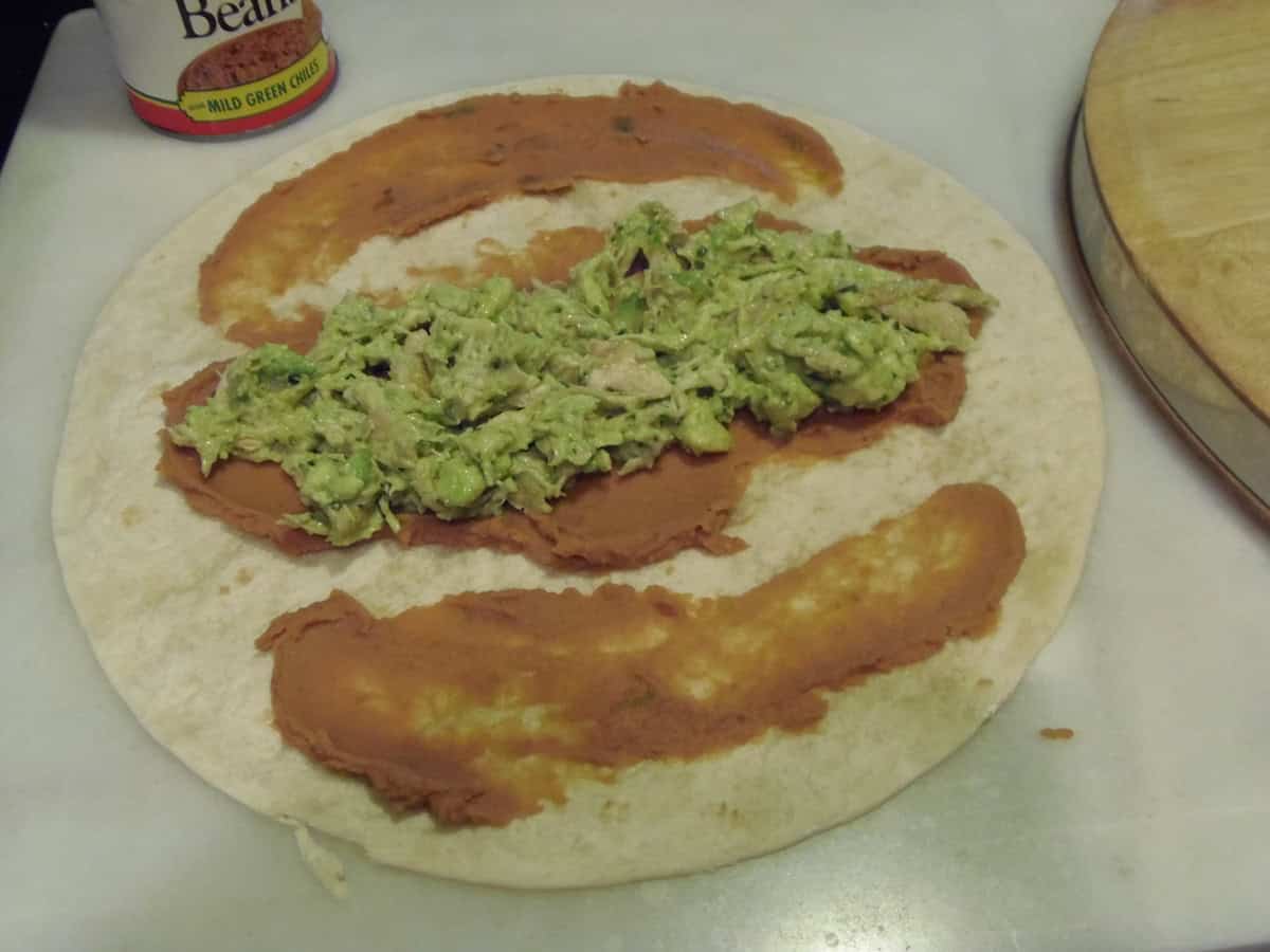 Refried beans and chicken mixed with avocado spread on a flour tortilla.