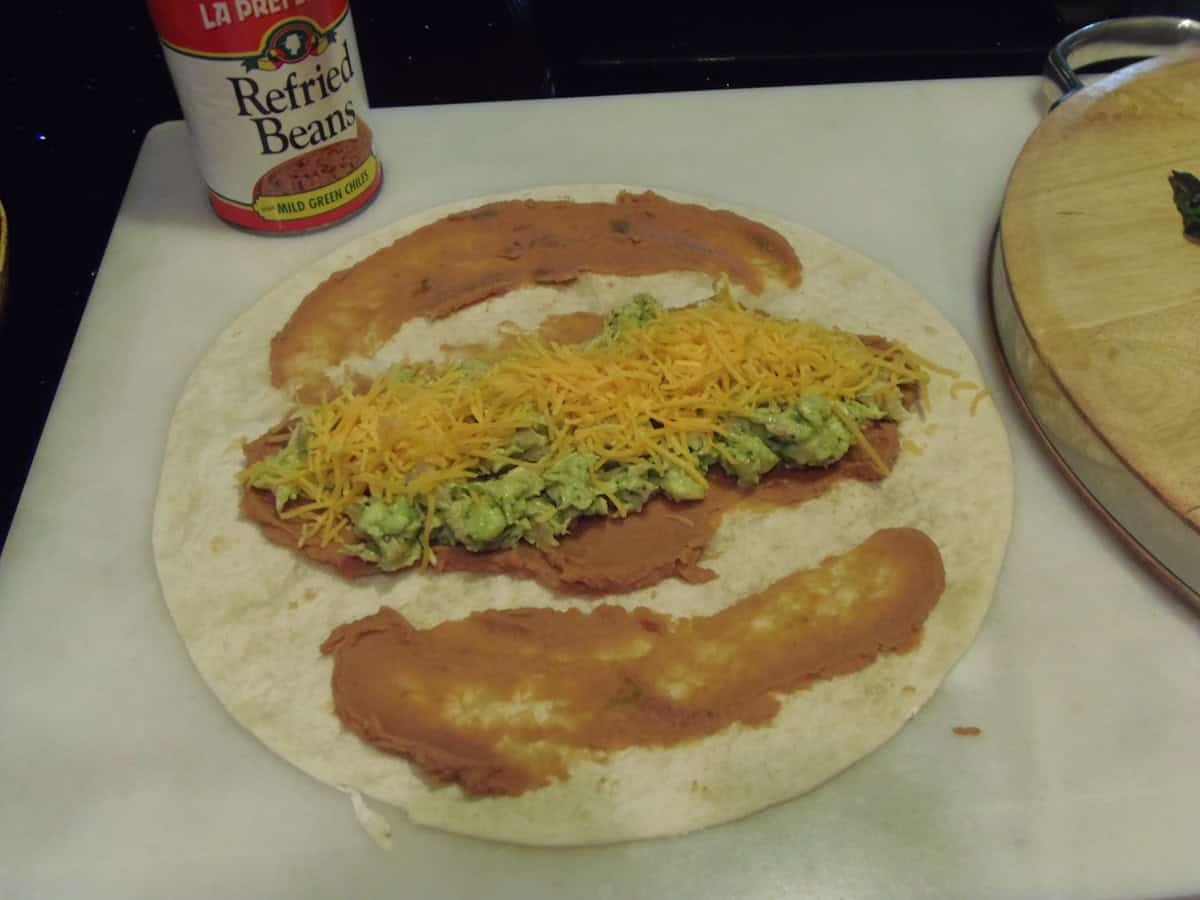 A flour tortilla with beans, avocado, cheese, and chicken ready to be wrapped.