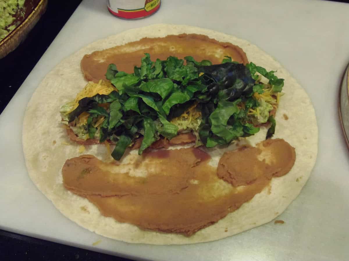 Refried beans, chicken, avocado and lettuce piled on a tortilla.