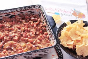 A square black and white baking dish filled with sausage bean dip with a bowl to dipping chips next to it.
