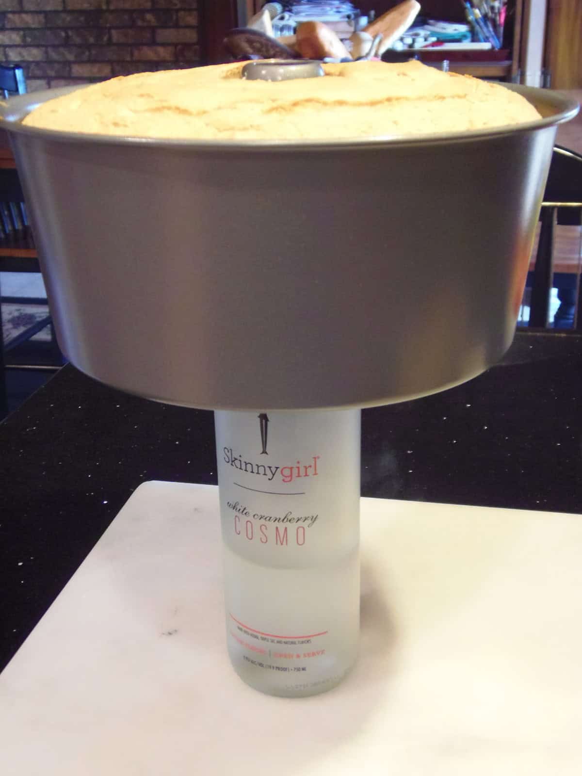 A baked angel food cake in a cake pan cooling on a bottle.