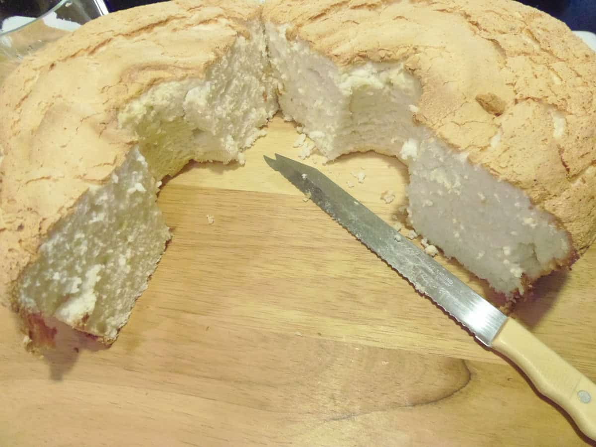 An angel food cake cut in half on a wooden cutting board.