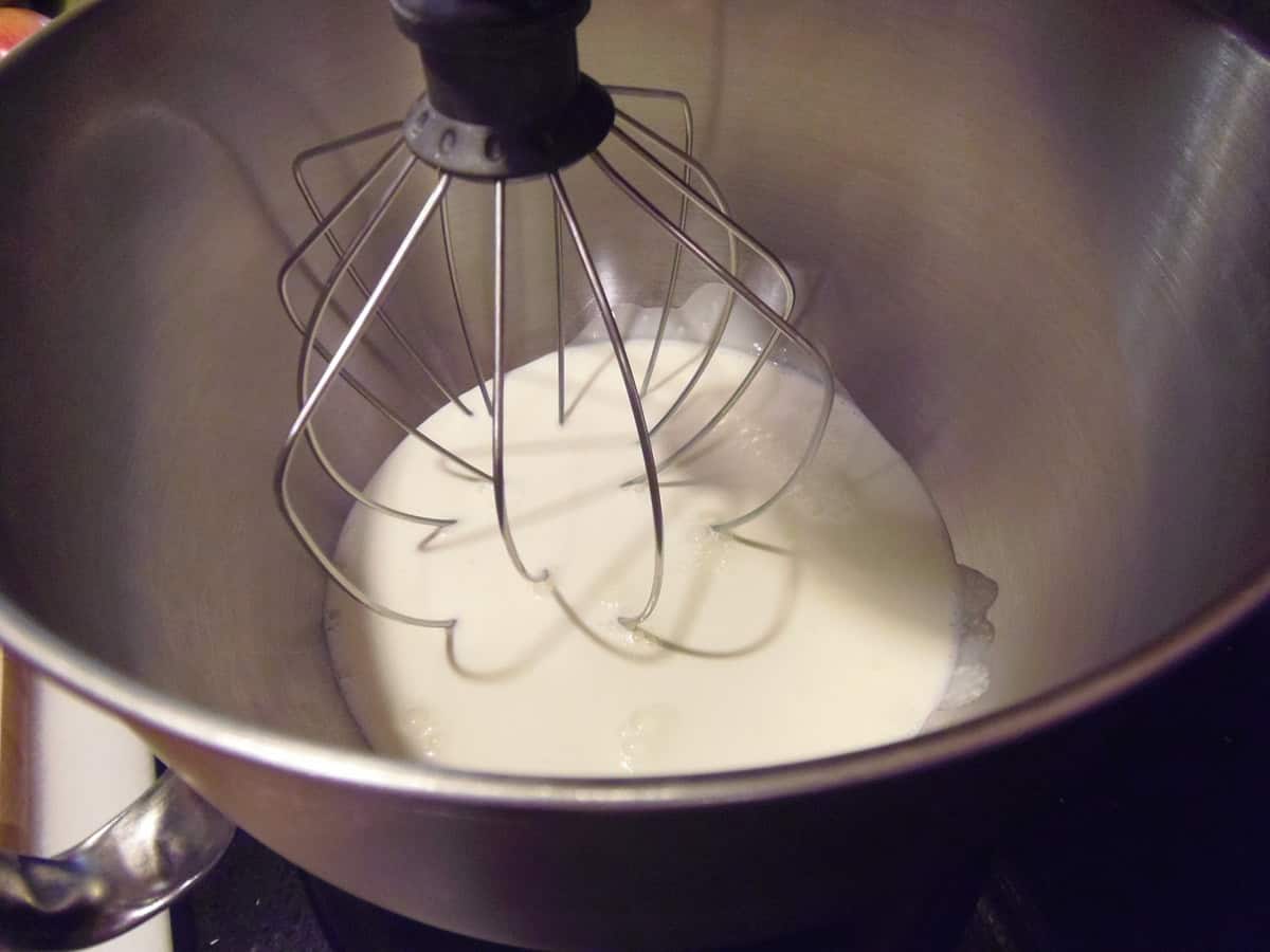 A whip in a stand mixing bowl with heavy cream.