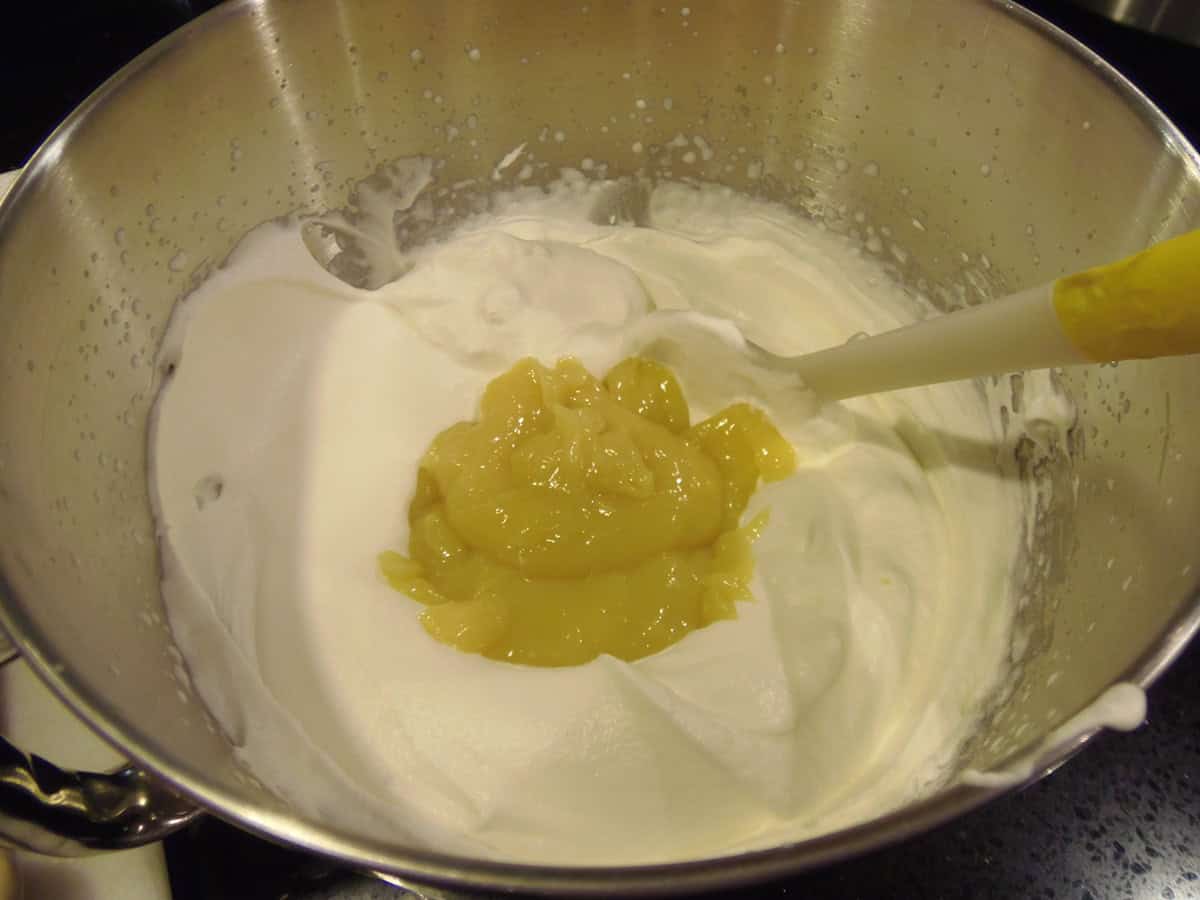 Lemon curd plopped in the middle of whipped cream in a mixing bowl.