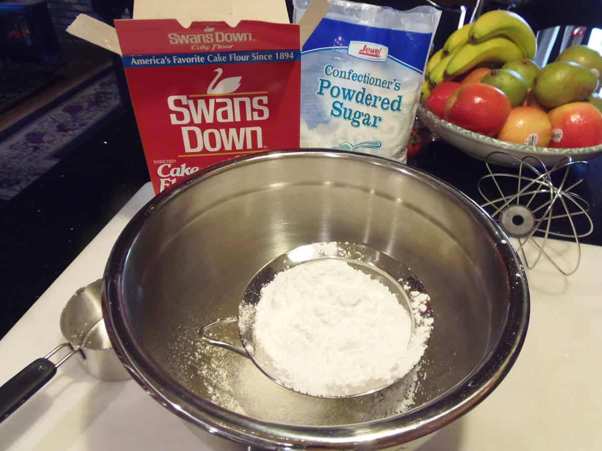 A sifter inside of a large mixing bowl filled with confectioners sugar.