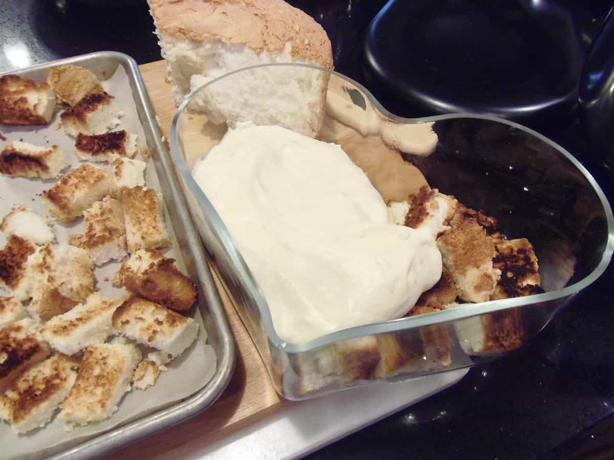 Cubes of golden angel food cake on a baking sheet with a heart shaped glass bowl next to it.