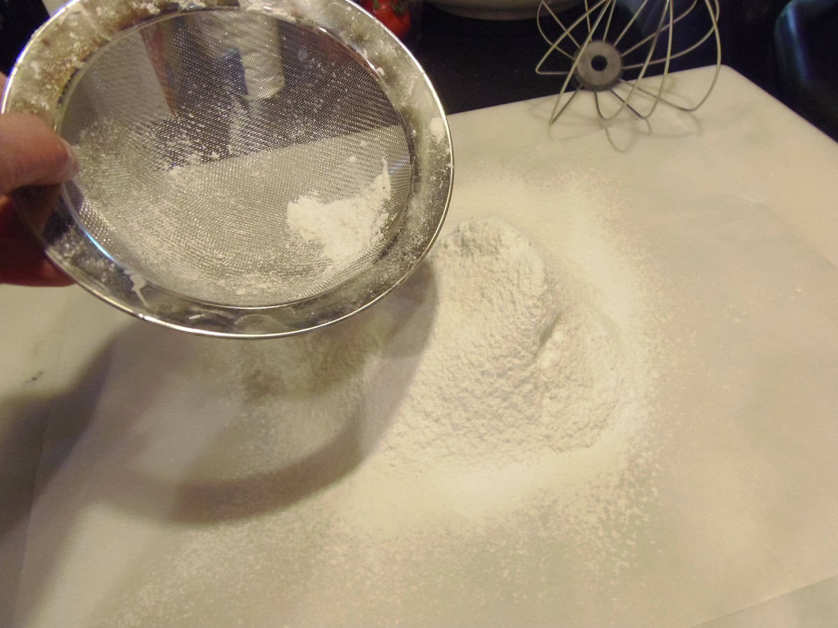 A fine mesh strainer sifting flour and sugar out onto parchment paper.