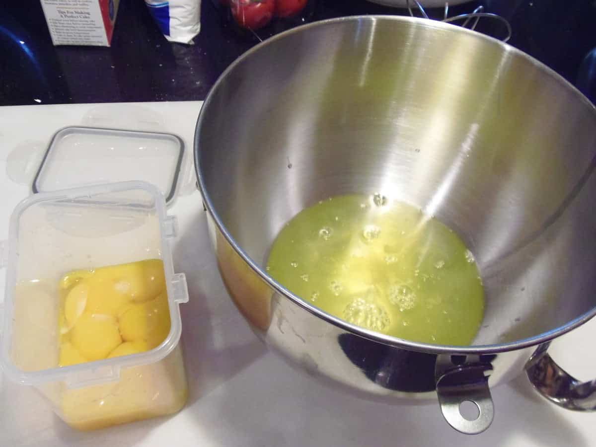 Egg whites in a stand mixer bowl with the egg yolks being in a small container for storage.