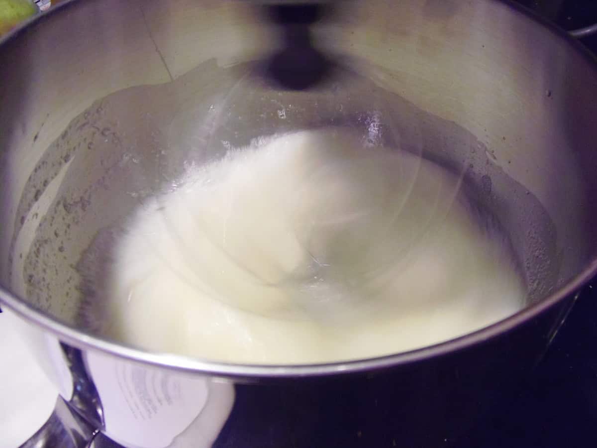 A whip in a stand mixer bowl beating egg whites to make an angel food cake.