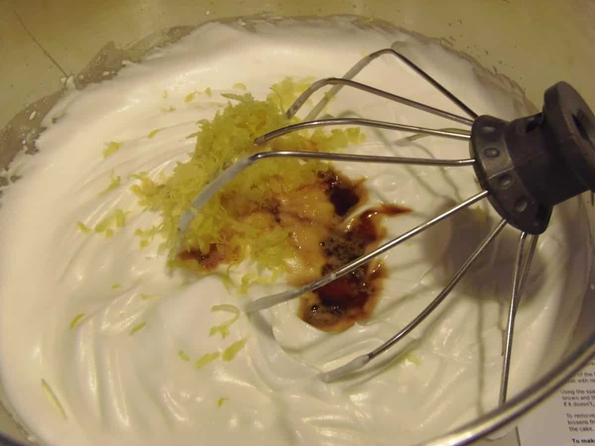 Whipped egg whites in a stand mixer bowl with lemon zest and vanilla extract.