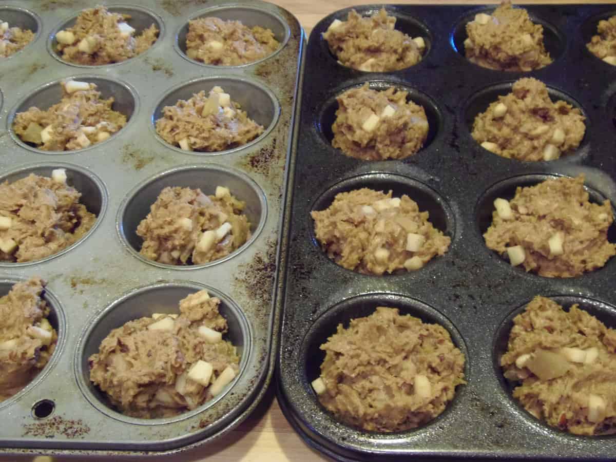 Two muffin tins filled with unbaked applesauce muffin scoops.