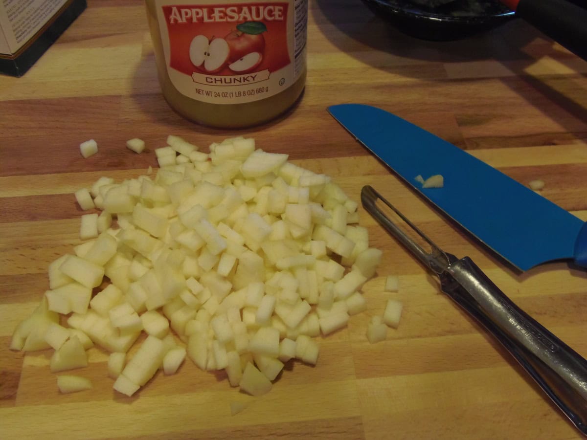 Diced apple on a wooden cutting board with a vegetable peeler.