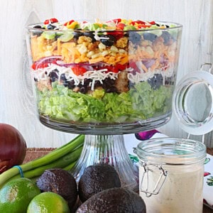 A layered chicken fajita salad in a glass bowl with lettuce, corn, olives, peppers, and lots of cheese.