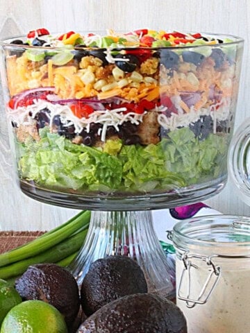 A layered chicken fajita salad in a glass bowl with lettuce, corn, olives, peppers, and lots of cheese.