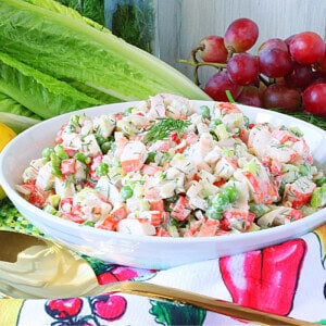 A colorful crab and pea salad topped with fresh dill in a white bowl.