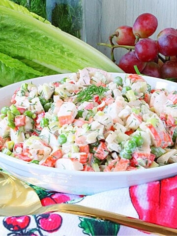 A colorful crab and pea salad topped with fresh dill in a white bowl.