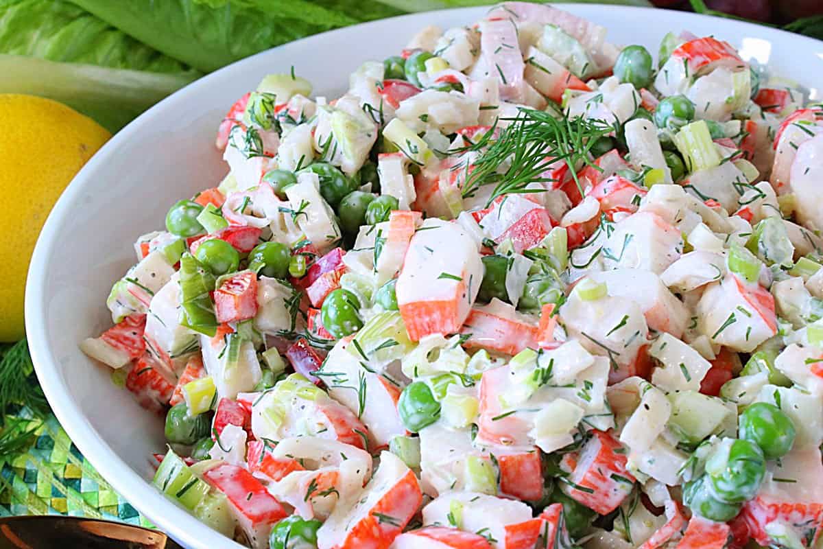 Chopped imitation crab legs, peas, and scallions served as a salad in a white bowl.
