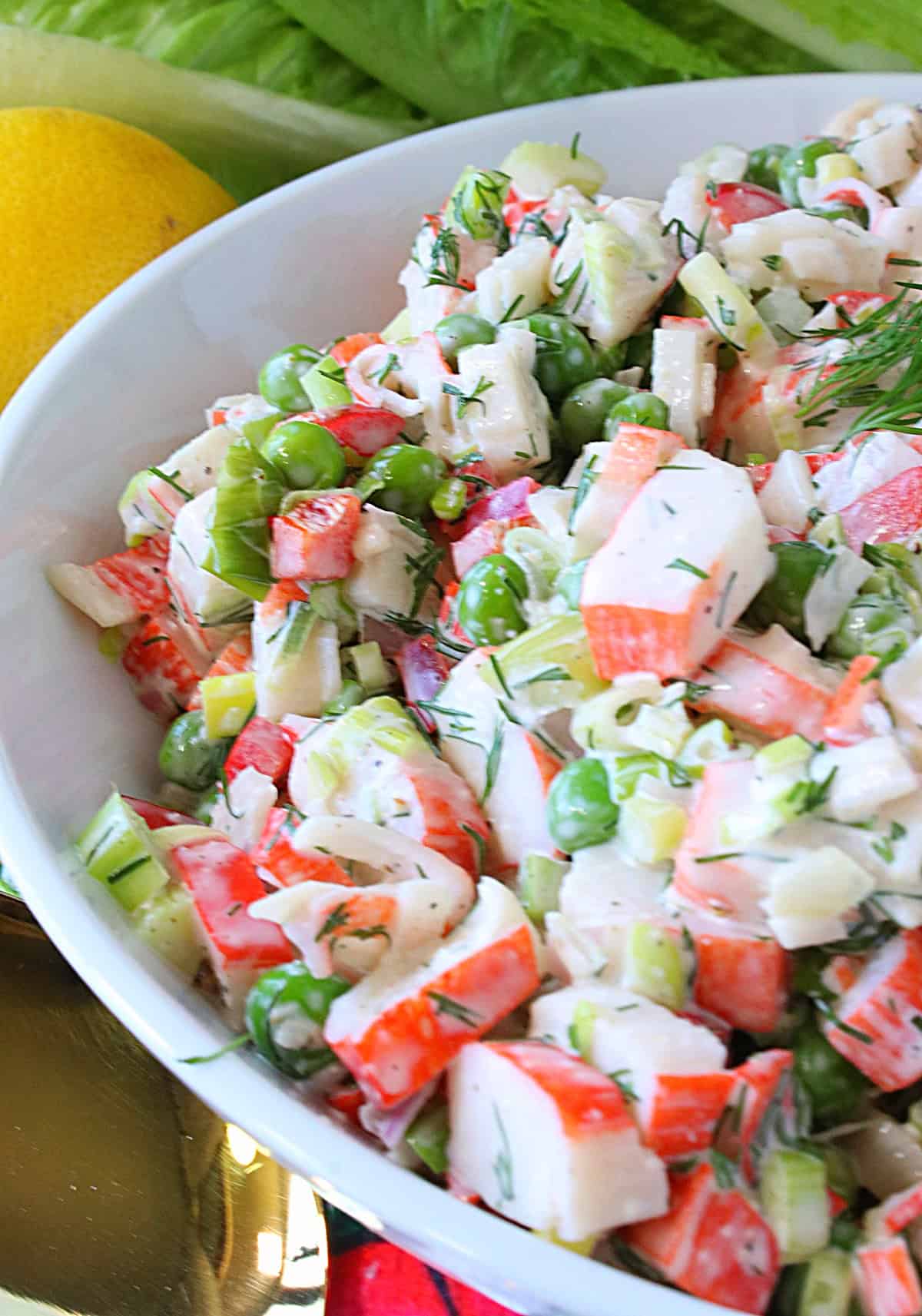 Chopped imitation crab, peas, scallions, mayonnaise, and dill as a crab salad in a white bowl.