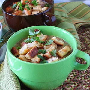 A bright green bowl with a handle filled with creamy Reuben soup and topped with rye bread croutons and fresh parsley.