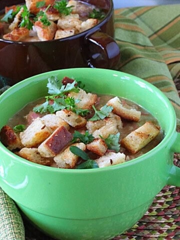 A bright green bowl with a handle filled with creamy Reuben soup and topped with rye bread croutons and fresh parsley.