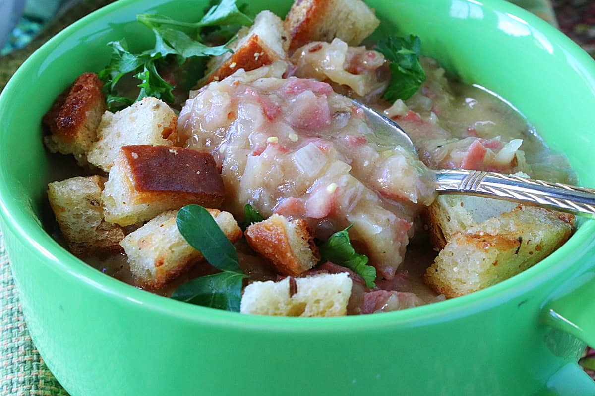 A spoon inside of a green bowl of Reuben soup showing the consistency of the soup.