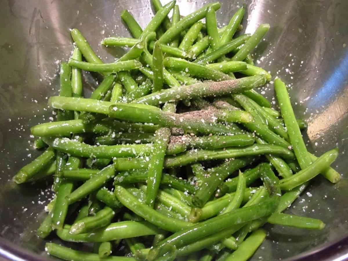 Green beans in a silver bowl with salt and pepper.