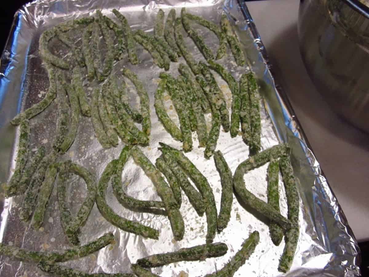 Potato flake coasted green beans laid out on a baking sheet covered with foil.