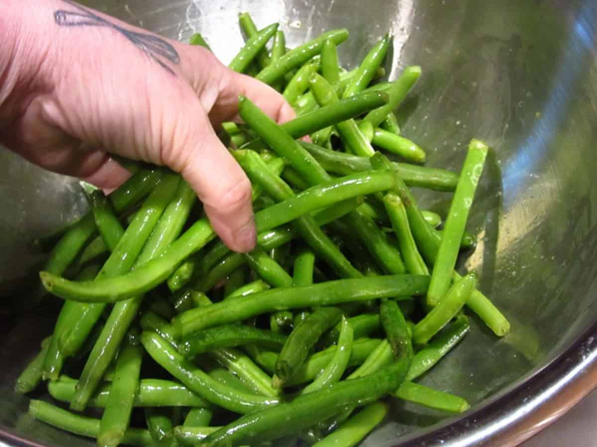A hand holding a bunch of green beans over a bowl.
